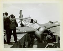 Photograph, Sailors aboard U.S.S. Rudyerd Bay looking at crashed FM2 aircraft on the portside catwalk.