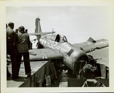 Photograph, Sailors aboard U.S.S. Rudyerd Bay looking at crashed FM2 aircraft on the portside catwalk.